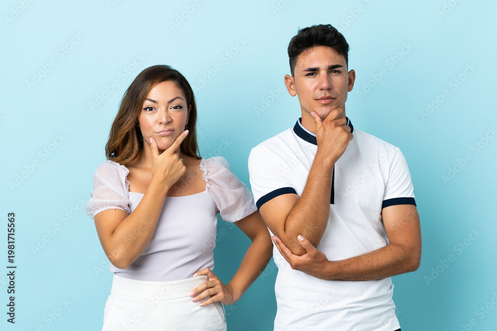 Fototapeta premium Young caucasian couple isolated on blue background having doubts and with confuse face expression