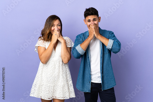 Фотография Young caucasian couple isolated on purple background smiling a lot while coverin