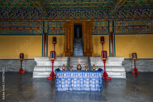 The ornate interior of a hall at Beijing's Temple of Heaven features a traditional ritual altar with bronze vessels and a golden shrine set against vibrant yellow walls.