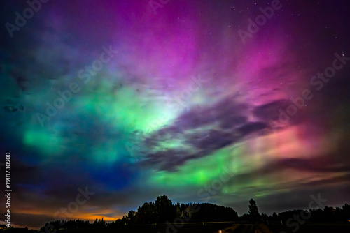 Northern öights dancing behinde the dark cloud over country landscape