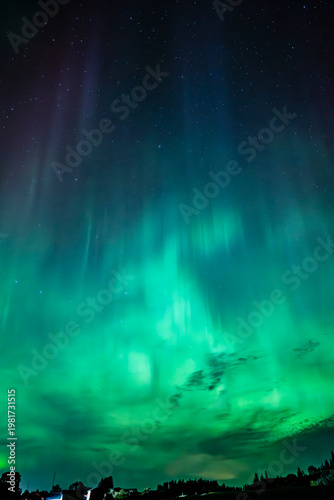 Northern öights dancing behinde the dark cloud over country landscape