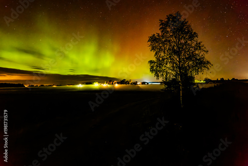 Northern öights dancing behinde the dark cloud over country landscape