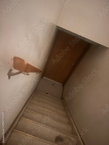 Narrow basement staircase leading downward with dim lighting showing confined residential interior and safety hazard concept