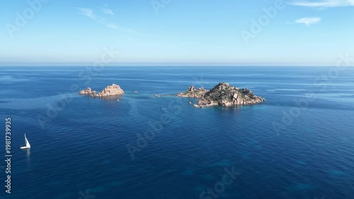 Aerial drone view of Santa Maria Navarrese, featuring turquoise waters, sandy beaches, marina harbor and dramatic limestone mountains along the eastern Sardinian coastline on a sunny day.