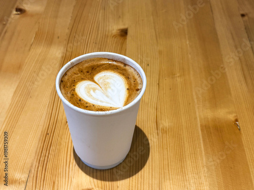 Coffee latte art on wood table in cafe nature light close-up. Cappuccino with a pattern in a paper cup on a wooden table in a coffee shop top view. The concept of food, drinks. Flat white art coffee. 