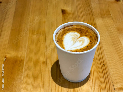 Coffee latte art on wood table in cafe nature light close-up. Cappuccino with a pattern in a paper cup on a wooden table in a coffee shop top view. The concept of food, drinks. Flat white art coffee. 