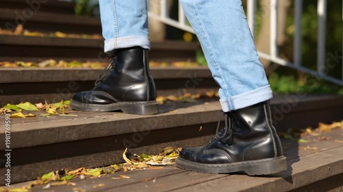 Guy in black boots going up the stairs in the park during sunny day. Leaves on the stairway. Cropped. Concept of autumn walks. Slow motion