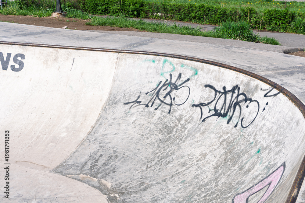 Naklejka premium Empty concrete skatepark ramp with black graffiti tags
