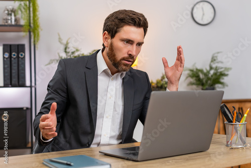 Middle-aged businessman at home office reads pay cut email on laptop and sighs after bad news sadly. Freelancer guy at table frowns thinking about salary cut and next steps for bills budget and rent.