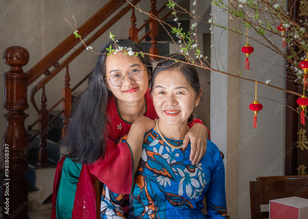Fototapeta premium Asian mother and daughter in traditional Ao Dai share a warm, affectionate moment. Lunar New Year, Mother's day, Woman's day, Birthday concept. Photo stock