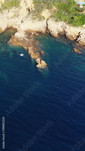 Aerial view of rugged rocks and crystal-clear turquoise water along the Calanques de Piana coastline in Corsica, France. Lush greenery tops the dramatic cliffs above the Mediterranean Sea.