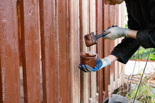 Painting wooden fence with brown paint during daytime