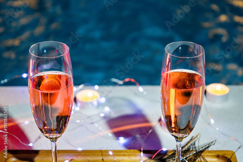 Two glasses of rose champagne by a luxury swimming pool at night