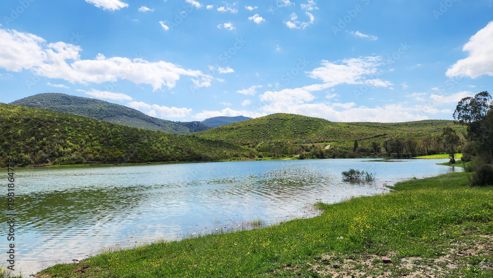 Fototapeta premium A scenic landscape featuring a calm lake surrounded by lush green hills and forests, reminiscent of natural areas found in Mediterranean climates