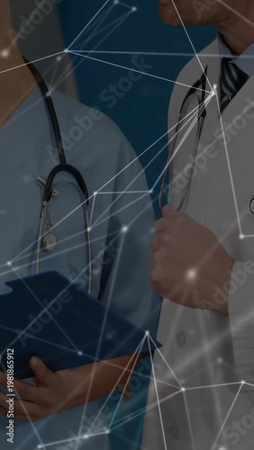 Vertical video: Reaching doctor in coat, nurse holding blue folder, reviewing in ward with overlay