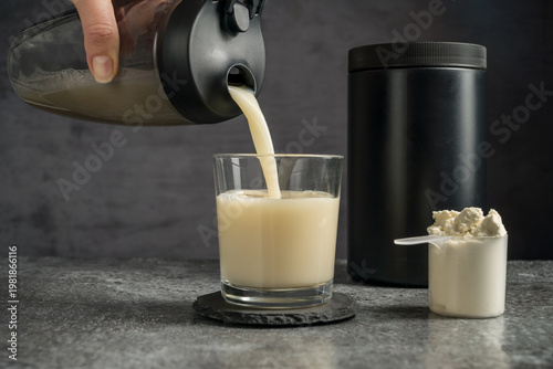 Bild auf Leinwand Pouring protein vanilla shake in drinking glass and scoop with whey protein powd
