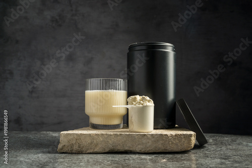 Protein shake in drinking glass and scoop with whey protein powder on dark background, copy space