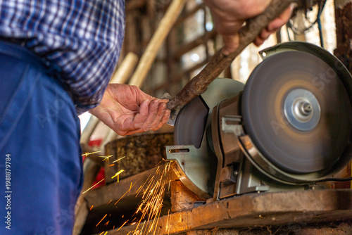 Foto Man sharpening metal tool on electric bench grinder, sparks flying from rotating abrasive wheel in workshop environment