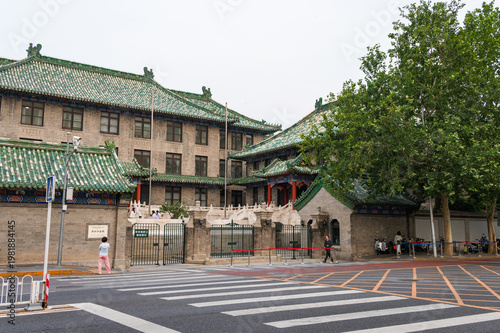 A historic building with distinctive green-tiled roofs stands at a city intersection in Beijing, traditional Chinese architectural elements and a pedestrian crosswalk. Beijing, China 29 May 2025