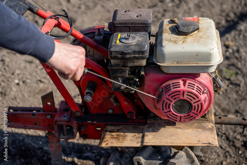 Photography Person pulling recoil starter cord on gasoline engine of walk behind tractor, starting agricultural machine on plowed field in daylight