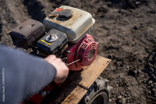 Photography Person pulling recoil starter cord on gasoline engine of walk behind tractor, starting agricultural machine on plowed field in daylight