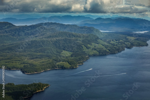 Aerial view of a vast Alaskan fjord with boats creating white wakes through the deep blue water
