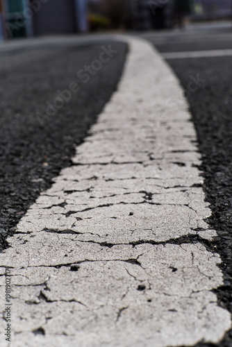 Weathered White Line with Cracks on Dark Asphalt Pavement, Close up View