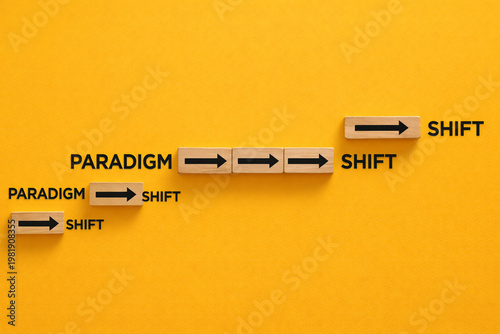 Wooden blocks with black arrows show a progression of the paradigm shift concept arranged in an ascending step pattern against a saturated yellow background for business.