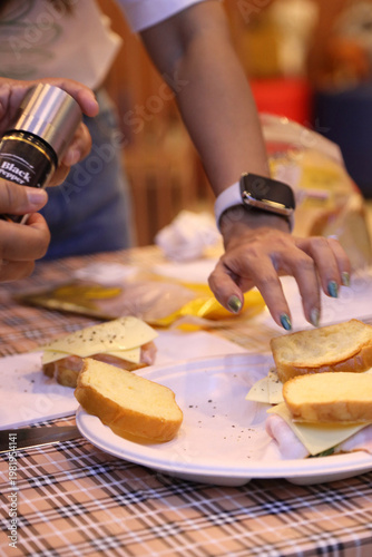 A female student in a cooking class reaching out to touch or pick up a gourmet sandwich she just prepared.