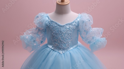 A child's elegant blue dress, featuring a beaded bodice and airy sleeves, on a pink background