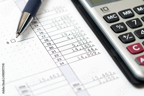A tax document with various numerical entries and lines, paired with a silver calculator and a blue ballpoint pen.