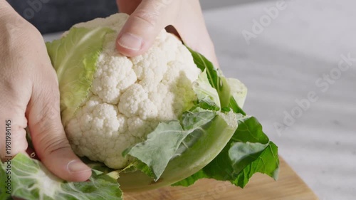 Hands holding fresh cauliflower with green leaves on a wooden cutting board. High quality 4k footage