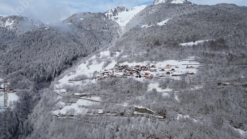Aerial view of a snowy alpine village with chalets in Tarentaise Valley surrounded by forest and mountains in the French Alps, Savoie, France.