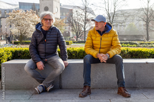 Two men sitting together on a stone bench in a city park enjoying conversation and friendship