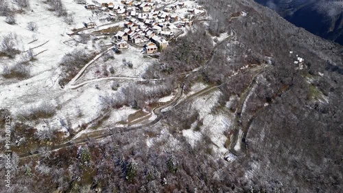 Aerial view of a snowy alpine village with chalets in Tarentaise Valley surrounded by forest and mountains in the French Alps, Savoie, France.