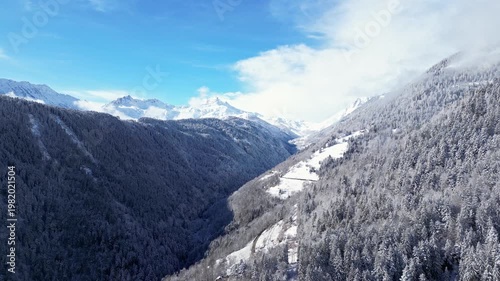 Aerial view of snowy Tarentaise Valley in the French Alps with fog, pine forests and dramatic winter mountains in Savoie, France.