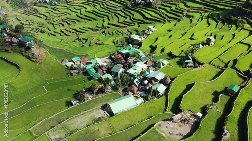 Aerial view of Batad village surrounded by lush green rice terraces in the Philippines. The landscape features dramatic terraced fields and traditional rural architecture.
