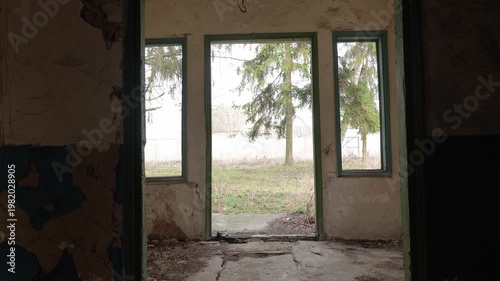 Interior View of Abandoned Dilapidated Building Looking Out Through Empty Doorway and Windows at Trees