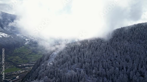Aerial view of Tarentaise Valley with highway, alpine villages and snowy mountains covered in fog in the French Alps, Savoie, France.