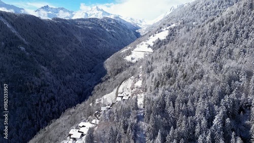 Aerial view of snowy Tarentaise Valley in the French Alps with fog, pine forests and dramatic winter mountains in Savoie, France.