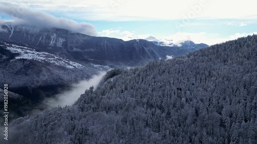 Aerial view of snowy Tarentaise Valley in the French Alps with fog, pine forests and dramatic winter mountains in Savoie, France.