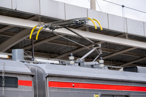 Photography Close-up of a commuter train pantograph mounted on a carriage roof, collecting electric current from overhead lines in an electrified railway system