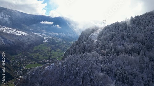 Aerial view of Tarentaise Valley with highway, alpine villages and snowy mountains covered in fog in the French Alps, Savoie, France.