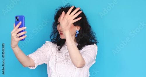 Excited Young Woman Having Emotional Video Call on Smartphone Gesturing with Hands and Laughing, Happy Female Blogger Recording Live Stream with Sincere Expression Isolated on Blue Background