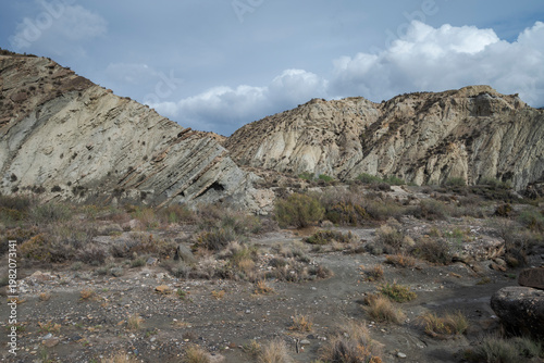 The arid landscape of Tabernas Desert in Almeria, Spain, with rugged hills, sparse vegetation, and rocky outcrops under a cloudy sky. It’s a popular filming location