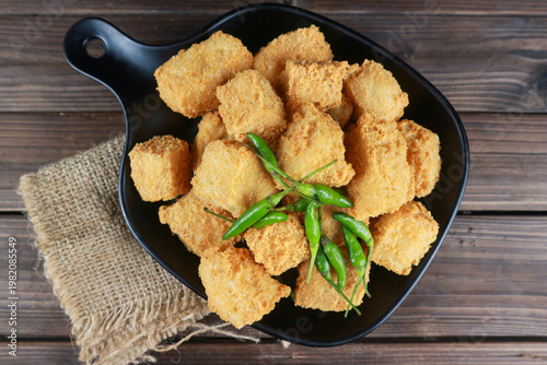 Crispy fried tofu tahu Sumedang in black plate with green chilies on wooden table.