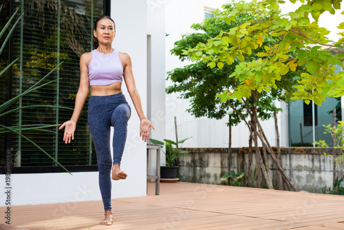 Fotografia Senior woman age 62 practicing yoga outdoors standing on one leg with other bent