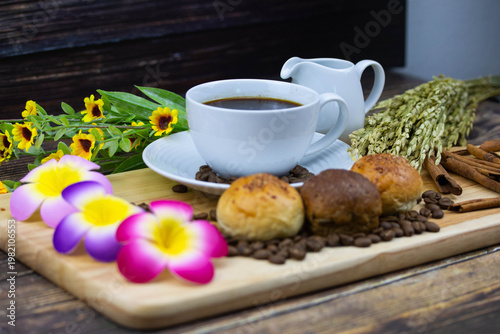Still life coffee scene with cup of black coffee, bread, coffee beans, sunflower and cinnamon on wooden background, warm cozy cafe