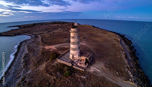 Aerial view of a historic striped lighthouse on a peninsula, ocean backdrop