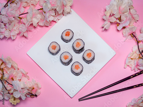 Hoso-Maki mit Lachs angerichtet vor einem rosa Hintergrund mit Blüten